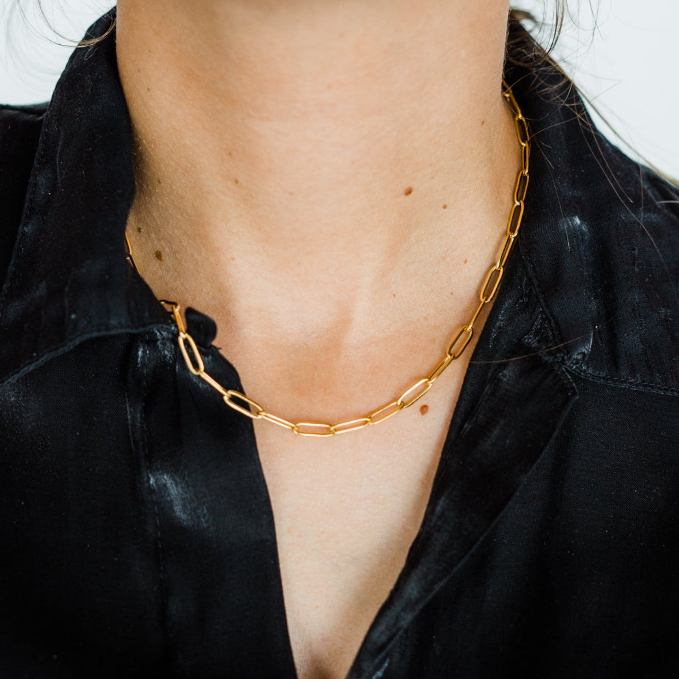 Close-up of a person wearing a gold necklace and earrings against a white background